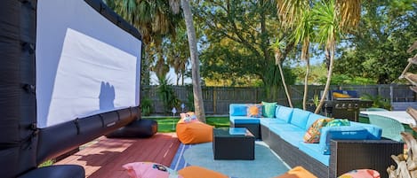 An outdoor patio with a large screen, seating area, and a grill.