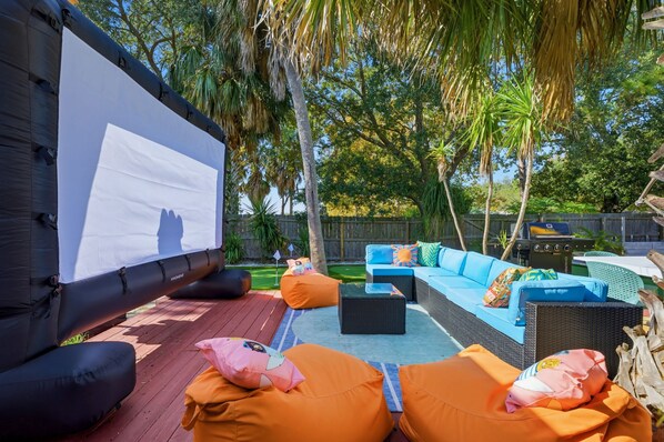 An outdoor patio with a large screen, seating area, and a grill. - Outdoor Movie Theatre Pool Putt Putt Hot Tub (Largo)