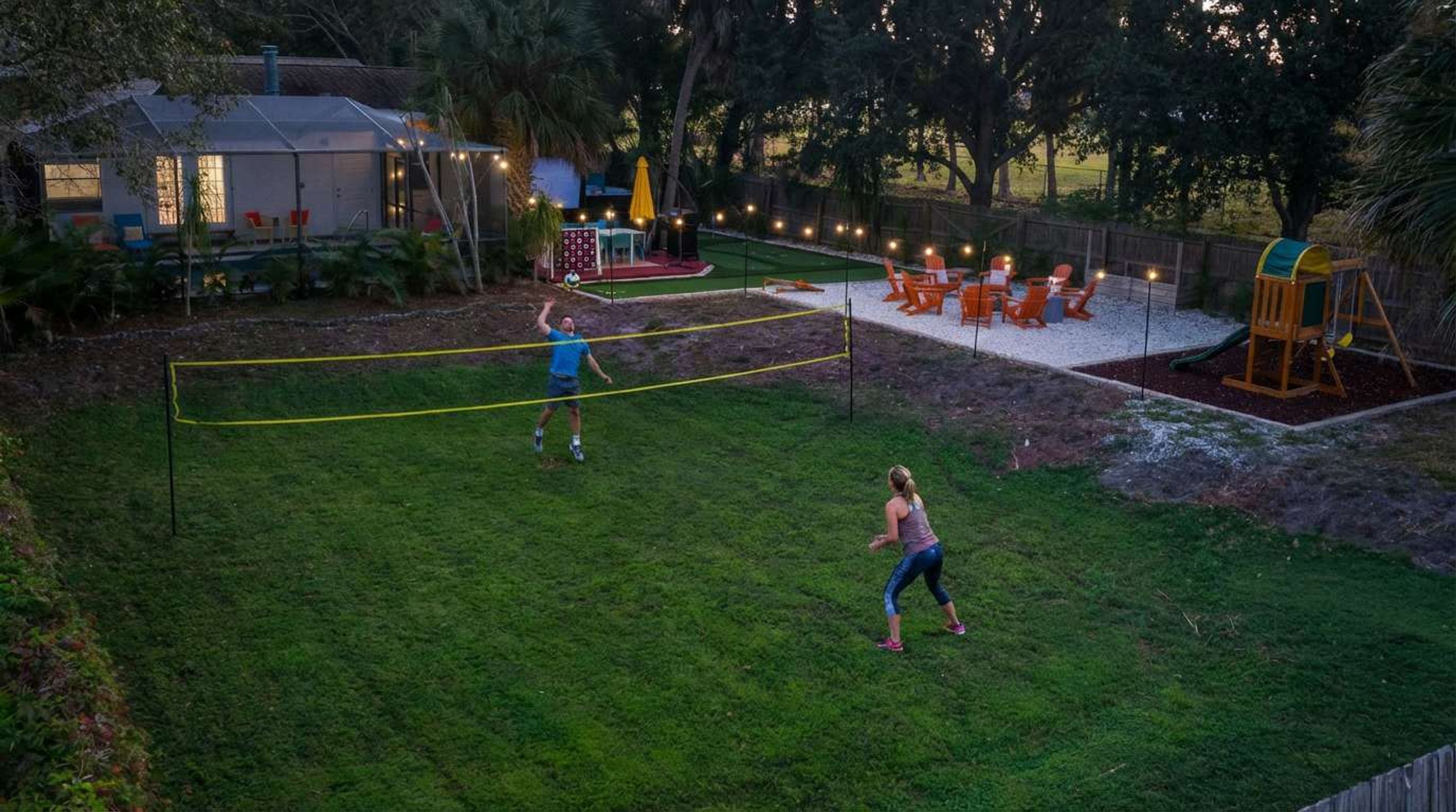 An outdoor area with a volleyball net, a swing set, and a fenced play area.