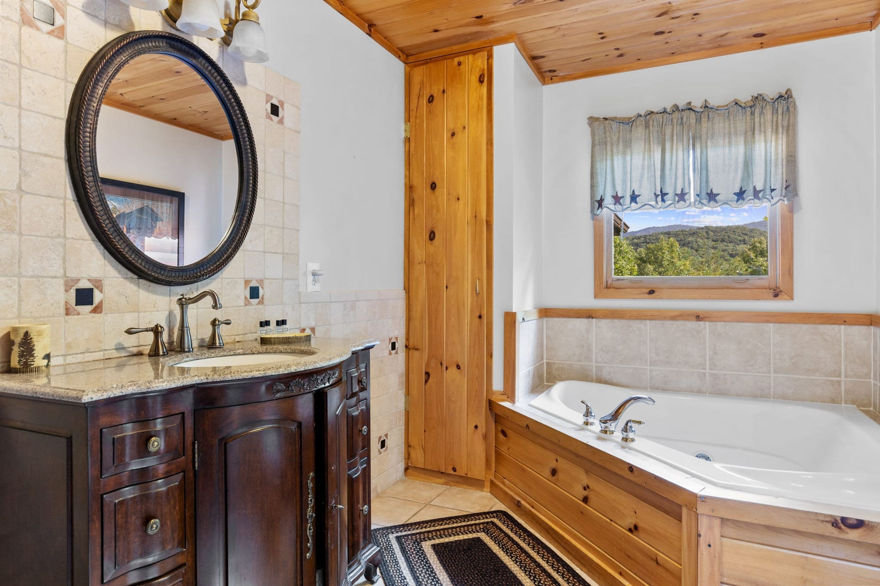 Un baño con tocador de madera, un espejo grande, una bañera y una ventana con vistas a un bosque.
