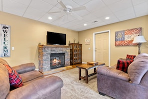 A living room with a stone fireplace, leather sofas, a flat-screen TV, and a ceiling fan. - Mountain Views Hot Tub Pool Table Firepit Games (Epworth)