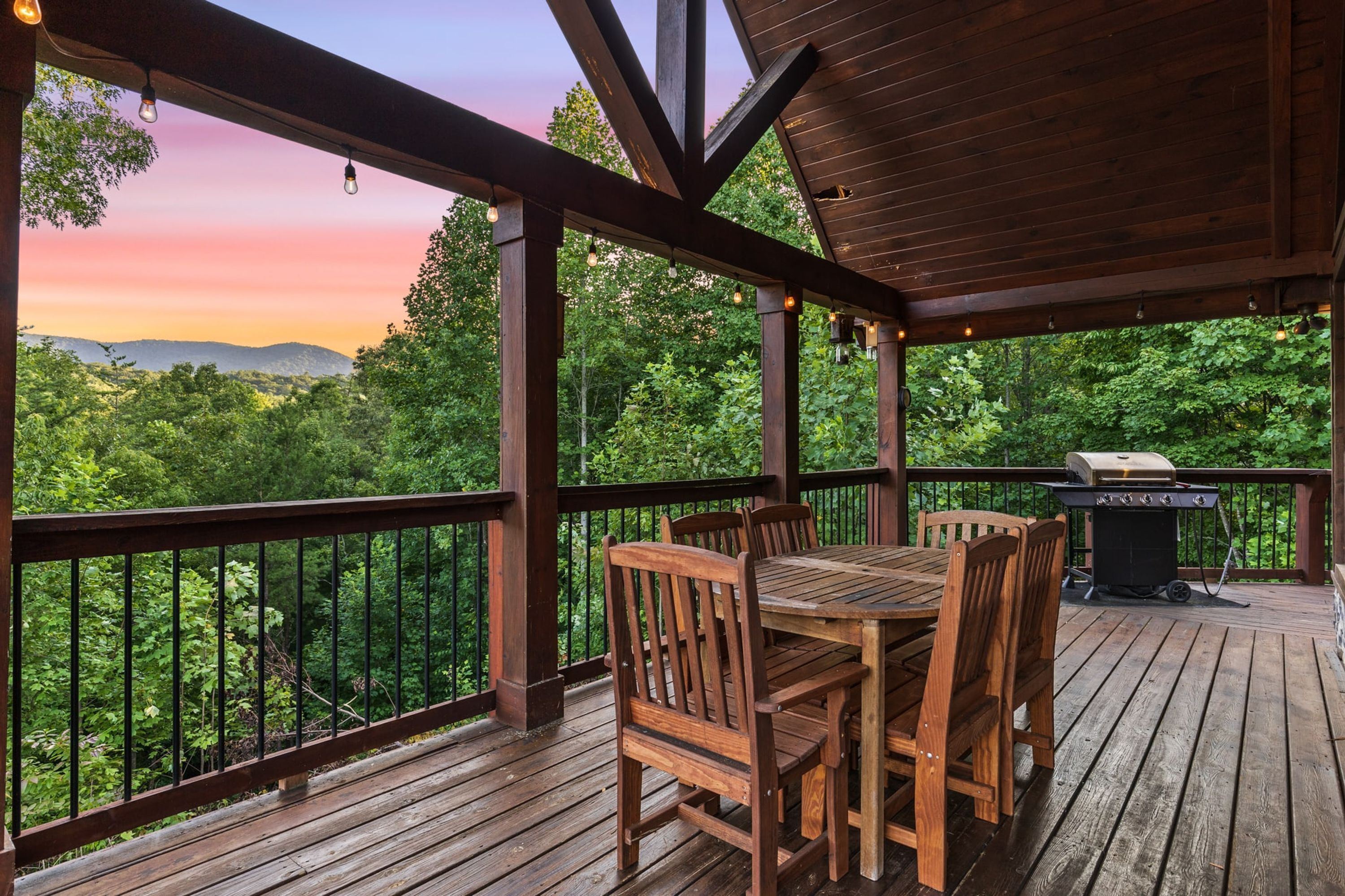 A wooden deck with a table and chairs, a grill, and a view of the forest.
