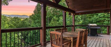 A wooden deck with a table and chairs, a grill, and a view of the forest.