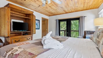 A bedroom with a bed, a television on a wooden cabinet, a window with curtains, and a ceiling fan.