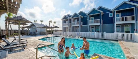 A swimming pool area with a pool, lounge chairs, and a building with balconies.