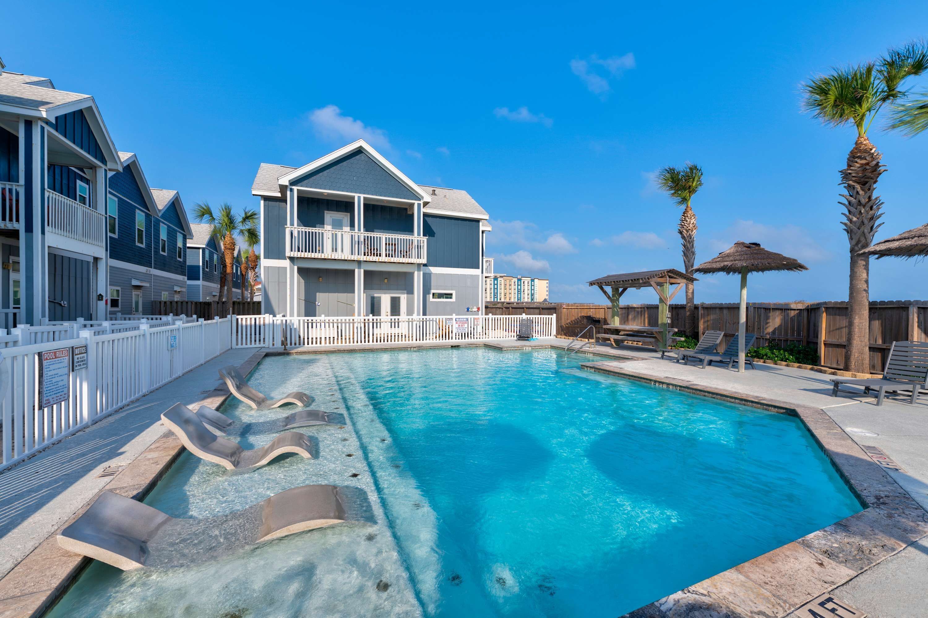 Une piscine avec des chaises longues, un bâtiment doté de balcons et des palmiers.
