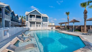 Une piscine avec des chaises longues, un bâtiment doté de balcons et des palmiers.