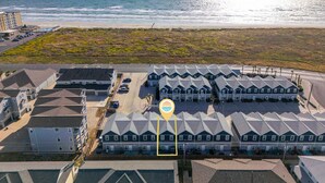 Une zone résidentielle côtière, avec une rangée de maisons, un parking et une plage en arrière-plan.