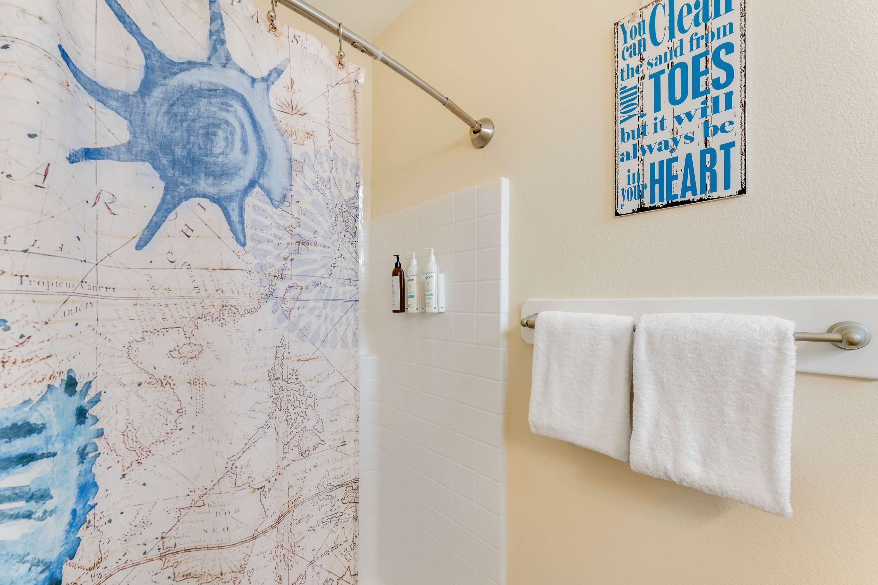 A bathroom with a shower curtain featuring a blue abstract design, a towel rack with two white towels, and a motivational quote on the wall.
