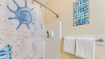 A bathroom with a shower curtain featuring a blue abstract design, a towel rack with two white towels, and a motivational quote on the wall.