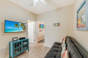 A living room with a flat-screen TV, a teal cabinet, a leather couch, and a hallway leading to another room. - Walk to Beach Private Hot Tub Pool Dog Friendly (Corpus Christi)