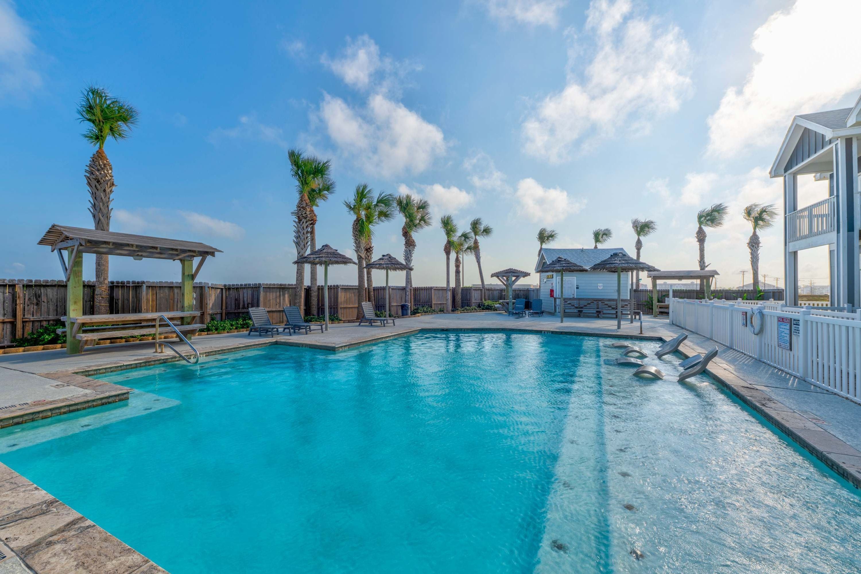 A swimming pool with lounge chairs and palm trees.