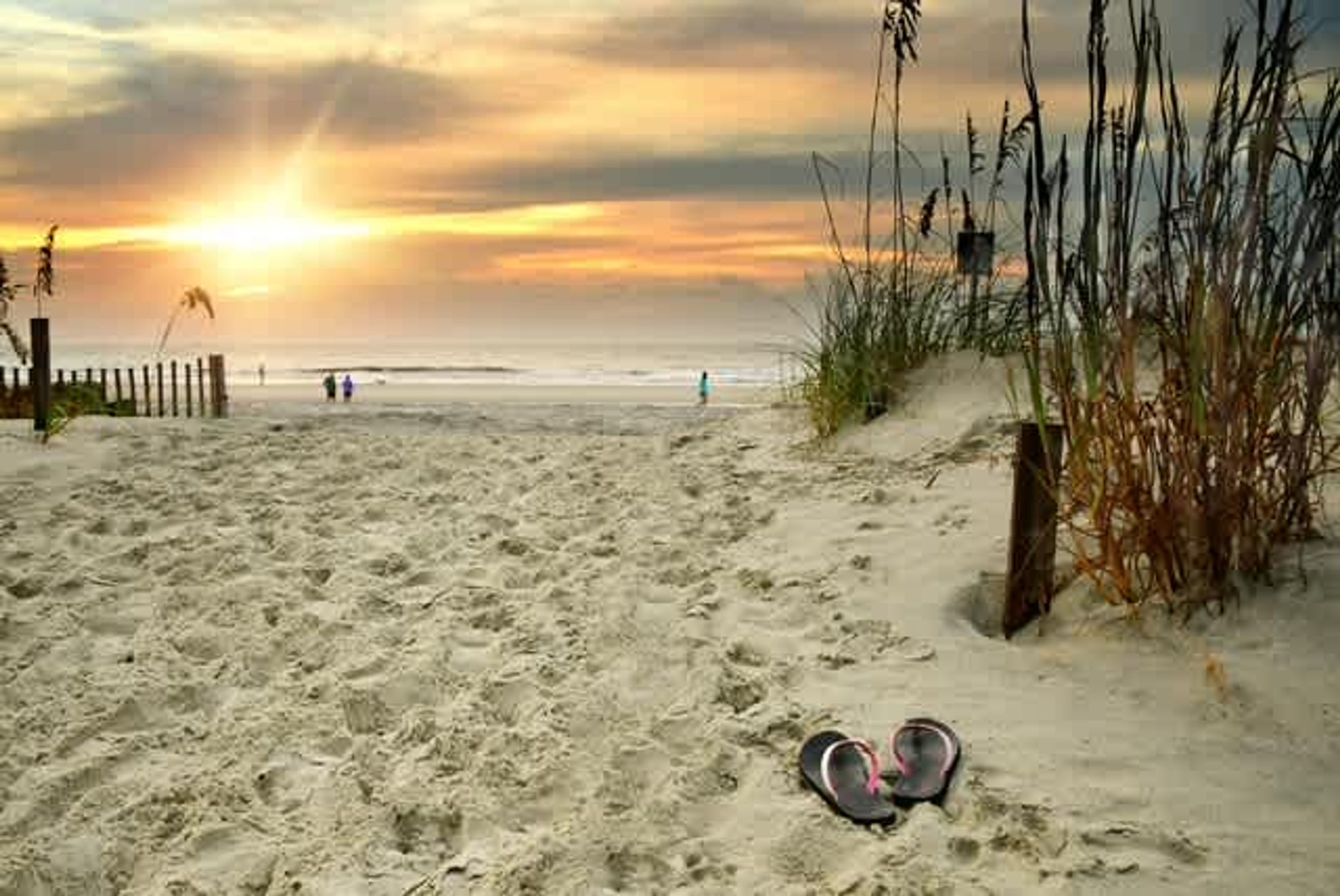 Ein Strand mit Fußspuren, die zum Wasser führen, einer Holzzahlung und hohem Gras.
