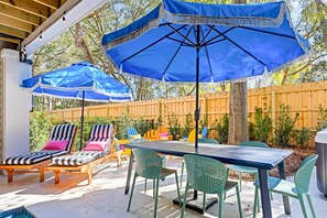 Eine Terrasse im Freien mit Tisch und Stühlen, blauen Sonnenschirmen und einem Holenzaun.