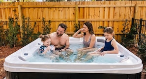 A family of four in a hot tub outdoors with a wooden fence in the background. - Hilton Head 6BR Sleeps 18 Pool Hot Tub Firepit (Hilton Head Island)