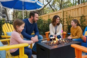 A family outdoors with a fire pit, yellow chairs, and an umbrella. - Hilton Head 6BR Sleeps 18 Pool Hot Tub Firepit (Hilton Head Island)