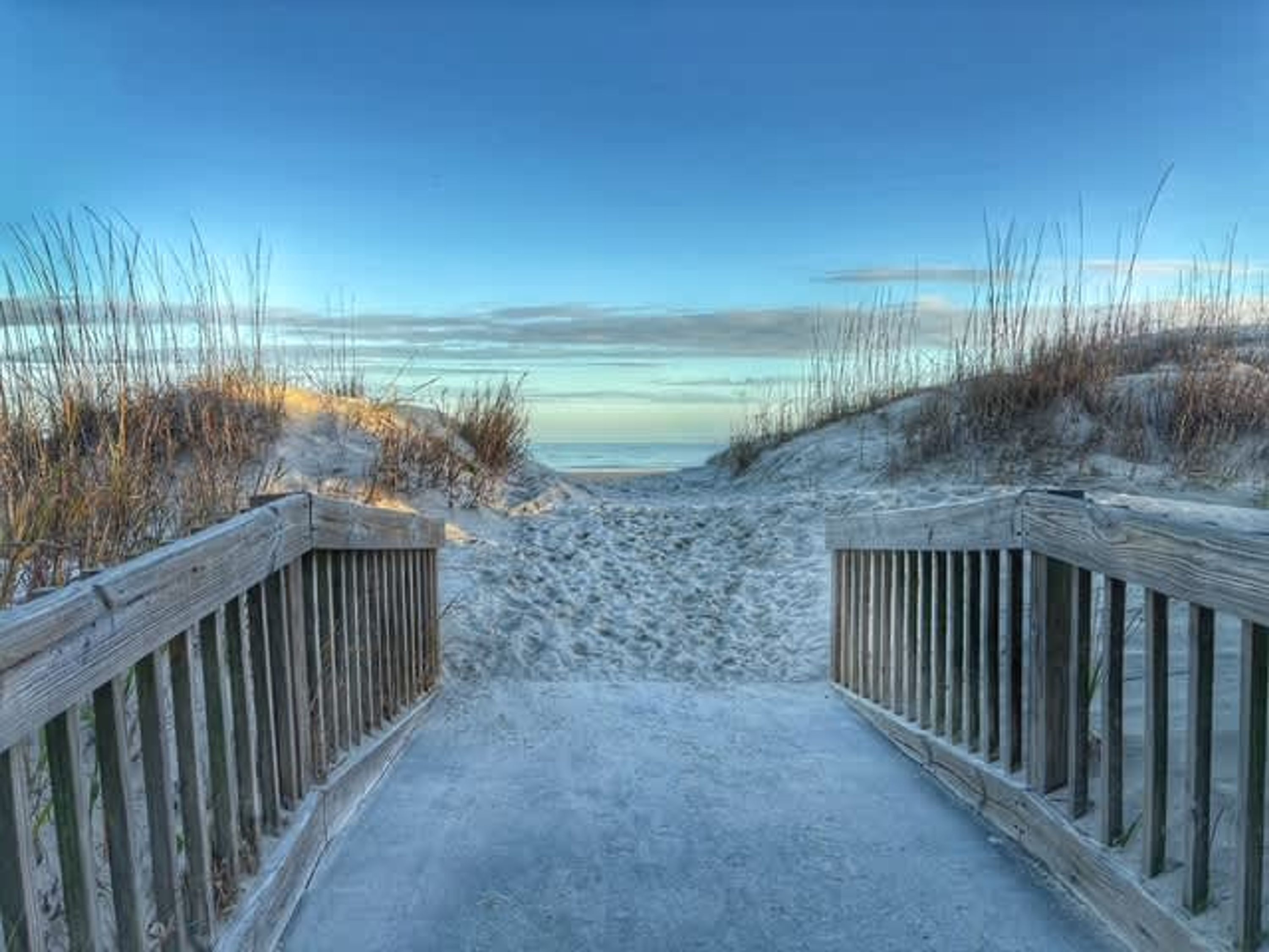 Une promenade en bois qui mène à une plage de sable où la végétation est clairsemée.