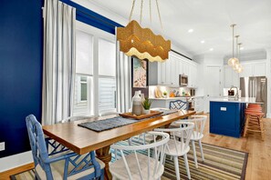 Eine moderne Küche mit weißen Schränken, einer blauen Kochinsel und einem Essbereich mit einem Holztisch und blauen Stühlen.