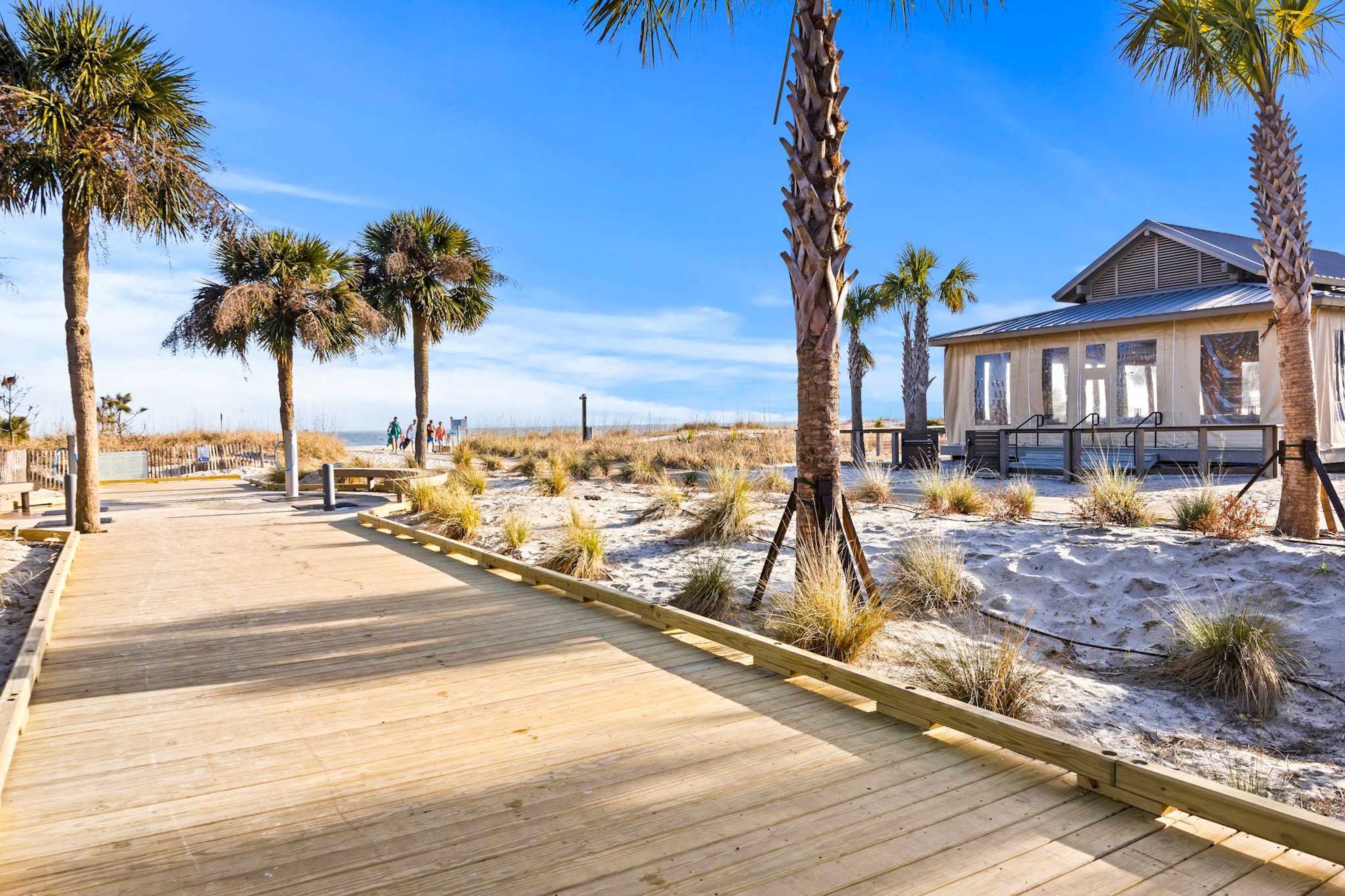 A wooden boardwalk leading to a building with a sandy beach and palm trees.