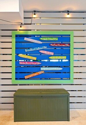 A wall with horizontal wooden slats and a colorful signboard displaying various locations with distances in miles. - Hilton Head 6BR Sleeps 18 Pool Hot Tub Firepit (Hilton Head Island)