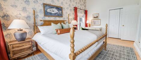 Une chambre à coucher avec un lit à baldaquin, une table de chevet, une lampe, une commode et une porte.