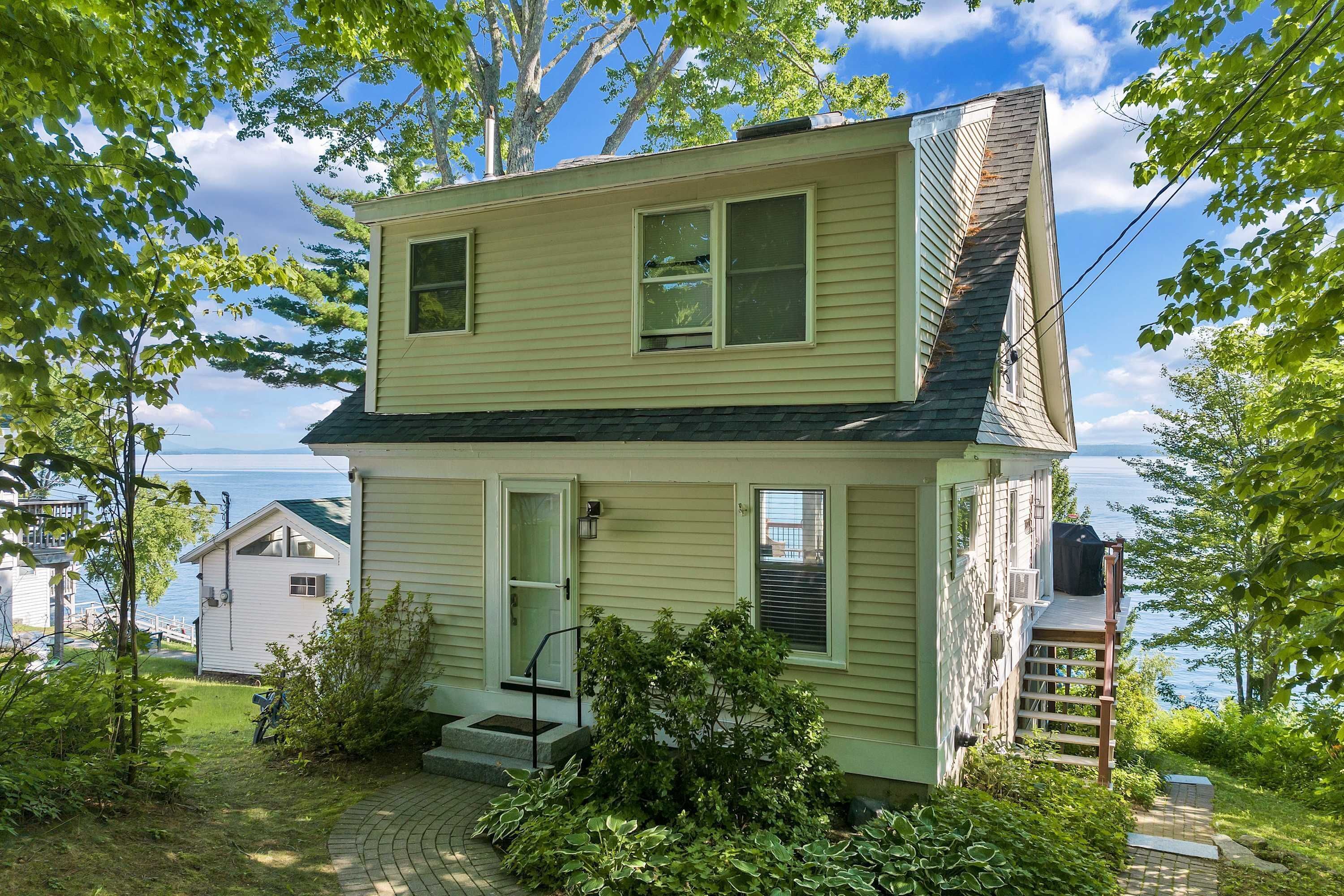 A two-story house with a front porch, a visible chimney, and a view of the water.