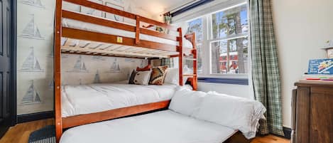 A bunk bed room with a window, a wall with sailboat wallpaper, and a bedside table with books.