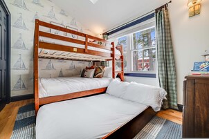 Habitación con literas, una ventana y una mesita de noche con libros. El papel tapiz de la pared muestra veleros.