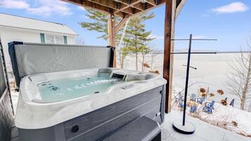 A hot tub under a wooden pergola with a view of a snowy landscape.
