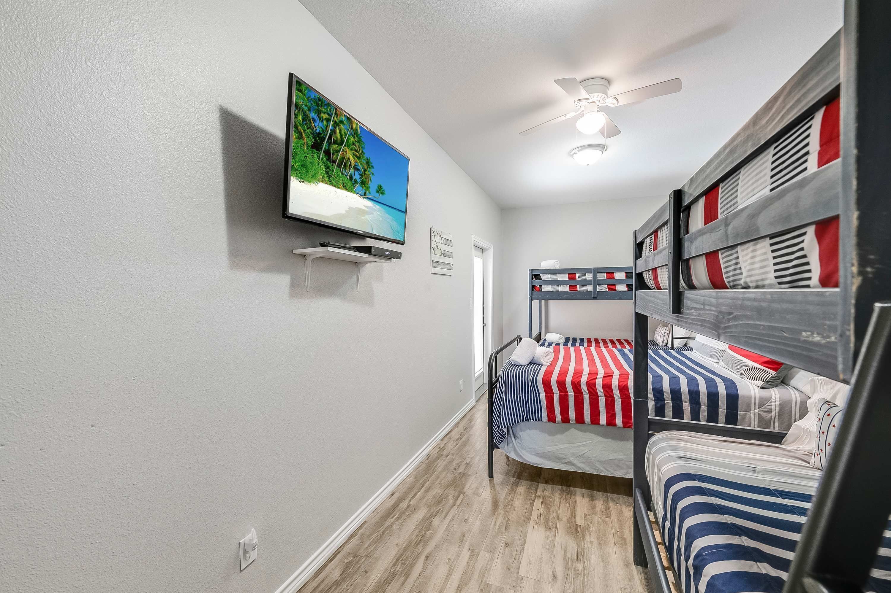 Une chambre avec des lits superposés, un téléviseur fixé au mur et un ventilateur de plafond.