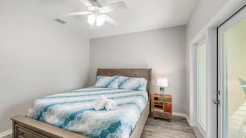 A bedroom with a bed, a nightstand, a lamp, a ceiling fan, and a door with blinds.