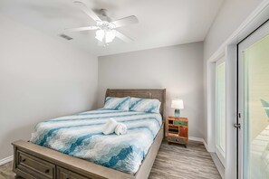 A bedroom with a bed, a nightstand, a lamp, a ceiling fan, and a door with blinds. - Cajun Shrimp Heated Resort Pool w Slide (Port Aransas)