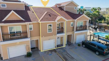 A multi-story residential building with a swimming pool, garage, and a vehicle parked in the driveway.