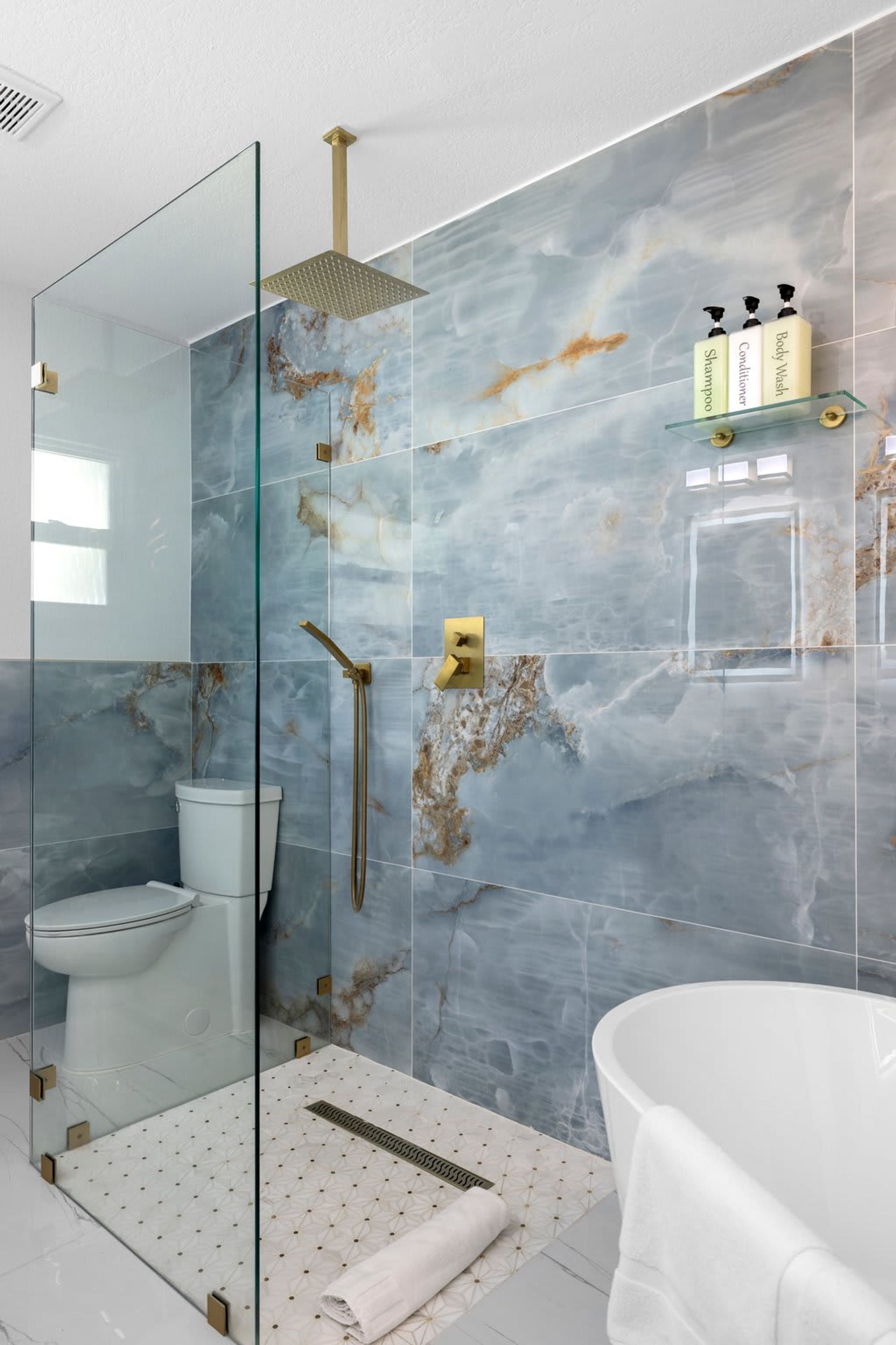 A modern bathroom with a glass shower enclosure, a white bathtub, and marble walls.