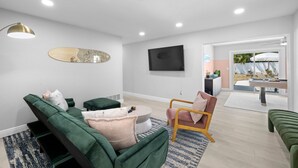 A modern living room with a green sofa, a small round table, and a TV mounted on the wall. - Sand Volleyball Pool Hot Tub 4BR Seminole FL (Seminole)
