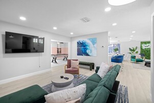 Una sala moderna con televisor de pantalla plana, mesa de billar y sofá verde.