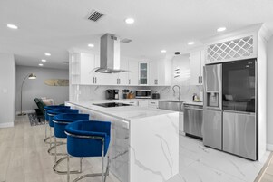 Una cocina moderna con una isla central, electrodomésticos de acero inoxidable y taburetes de bar azules.