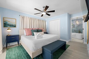 Un dormitorio con cama, mesita de noche, lámpara, ventilador de techo y un baño con bañera.