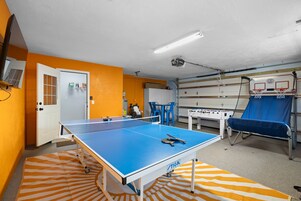 Una habitación con mesa de ping pong, mesa de fútbol y aro de baloncesto.