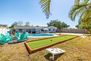 Un patio trasero con piscina, césped y cancha de bochas.