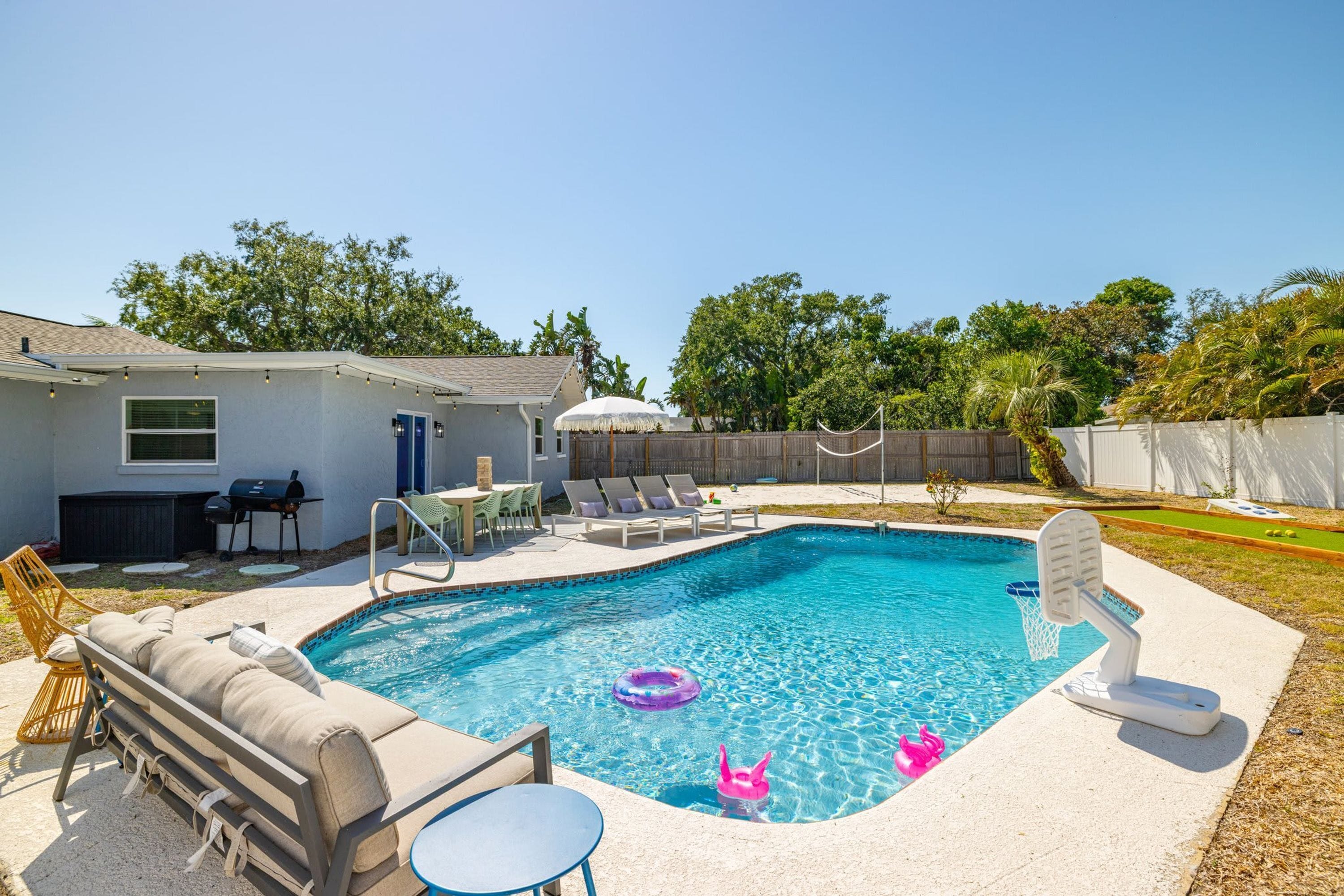 A backyard with a swimming pool, lounge chairs, a barbecue area, and a fenced yard.