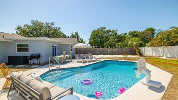 A backyard with a swimming pool, lounge chairs, a barbecue area, and a fenced yard.
