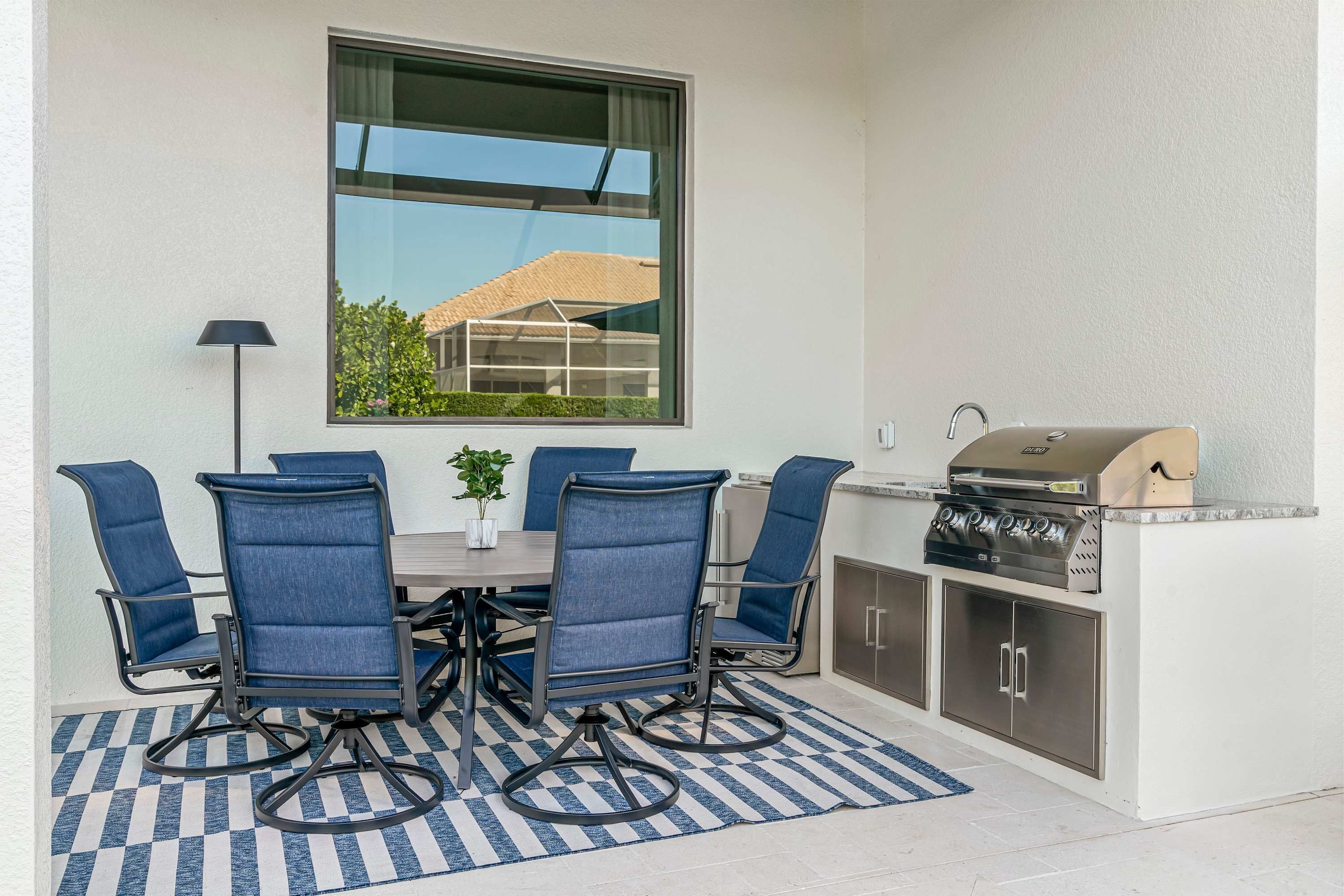Un patio al aire libre con una mesa, sillas, una parrilla y vistas a una casa a través de una ventana.