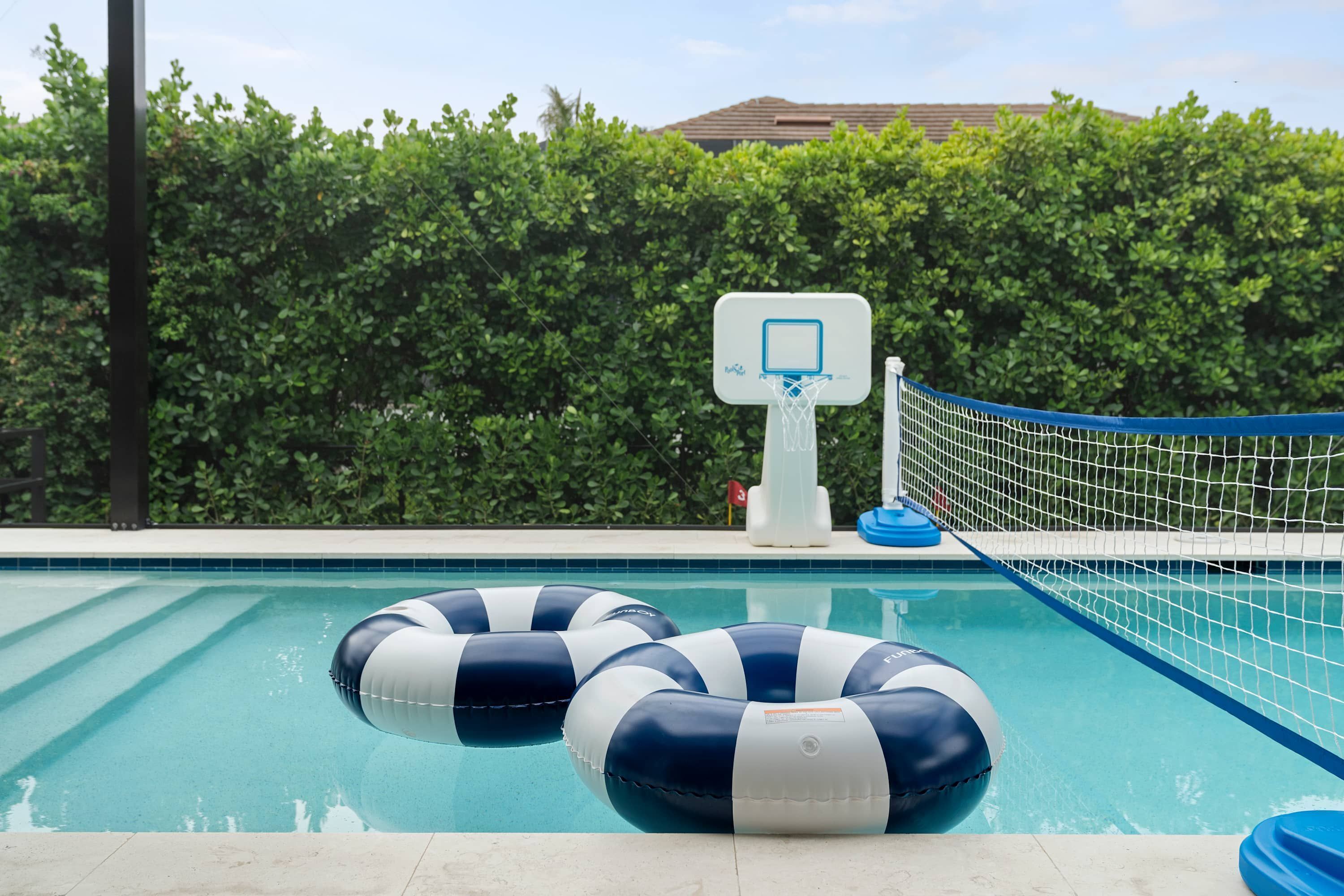 A swimming pool with a basketball hoop and two inflatable rings.