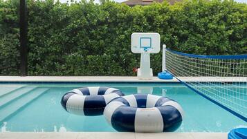 A swimming pool with a basketball hoop and two inflatable rings.