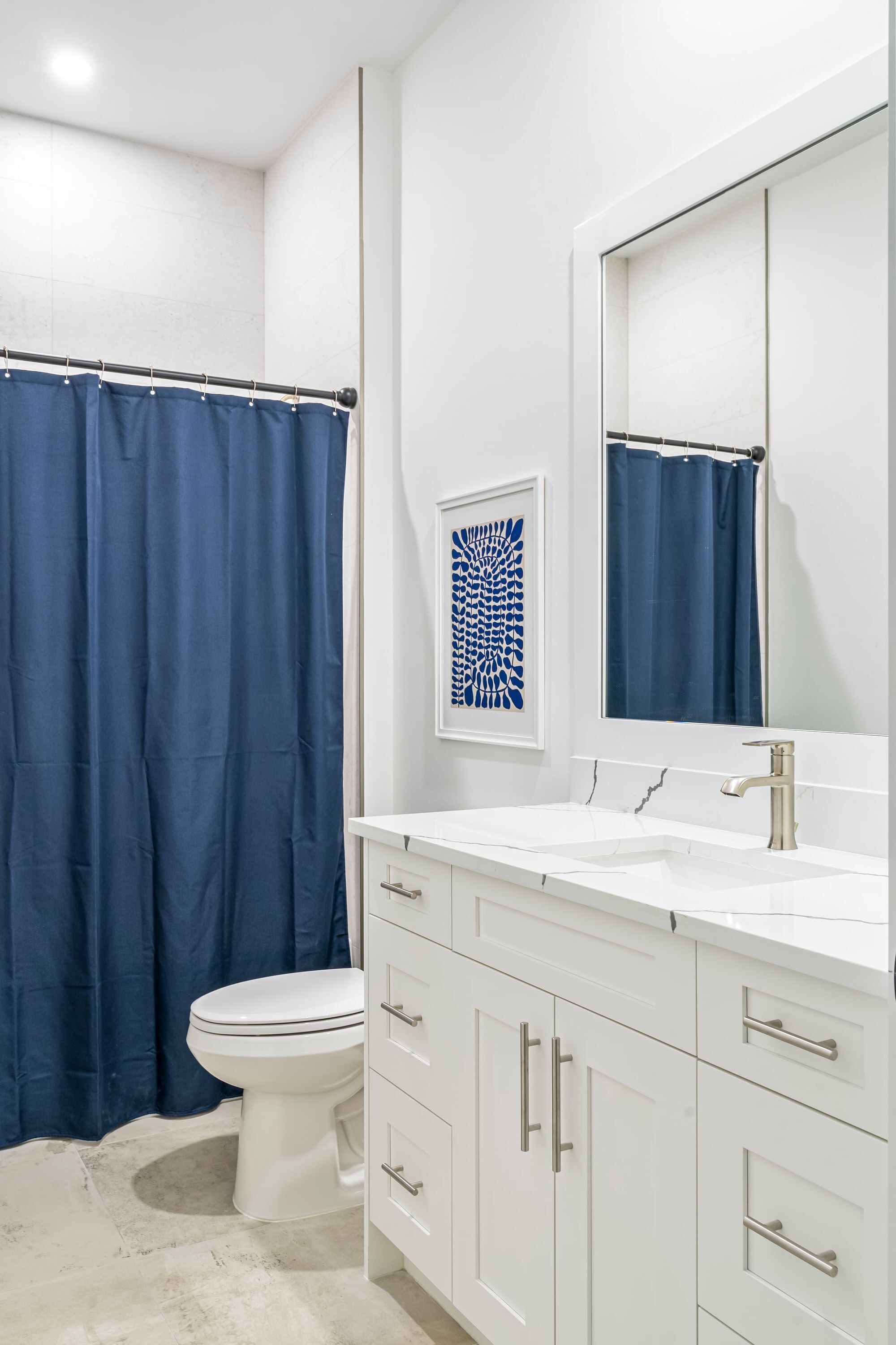 Un baño con lavamanos blanco, espejo, inodoro y cortina de ducha azul.