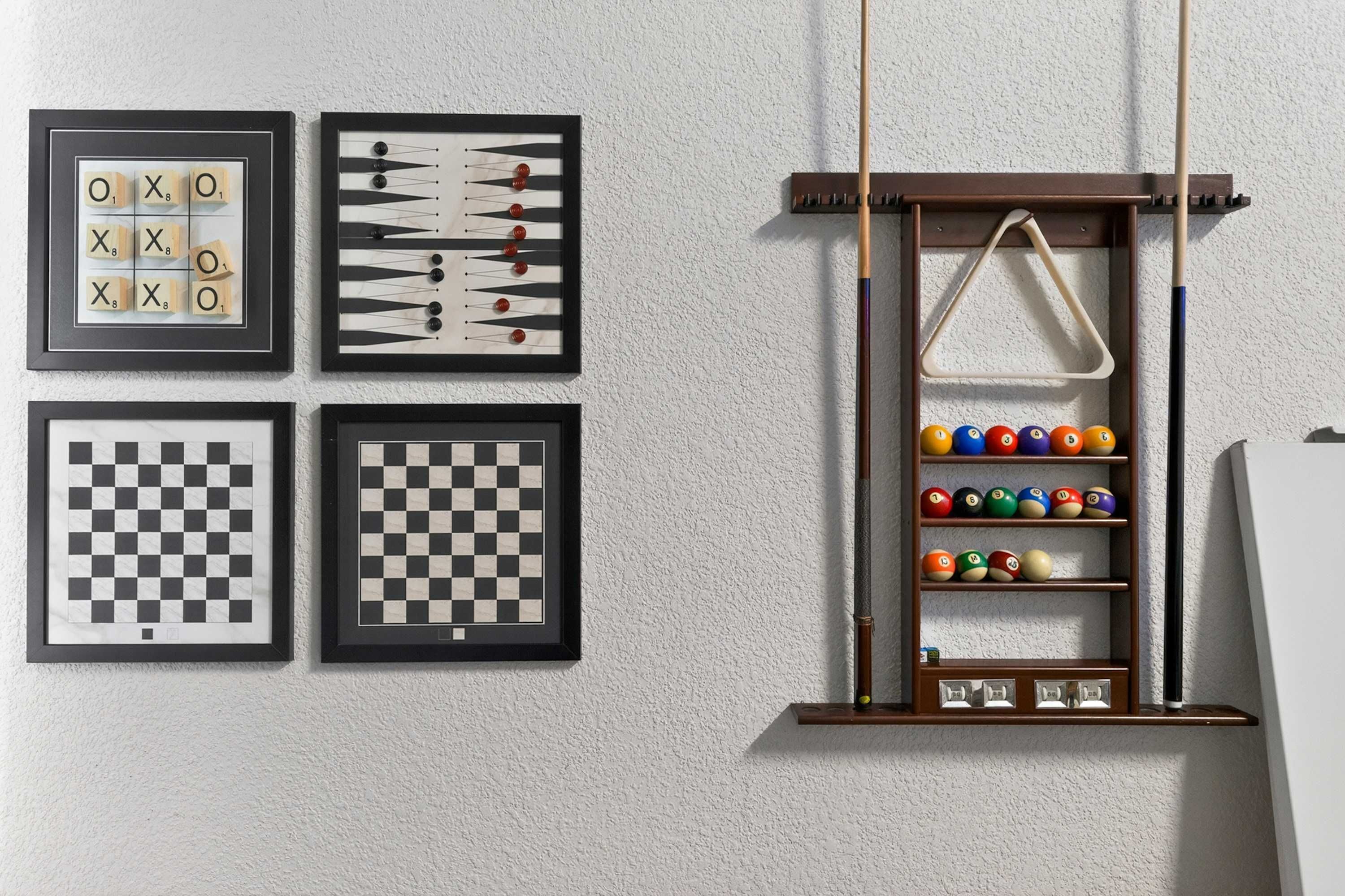 A wall with four framed board games, a billiards rack, and a set of billiard balls.