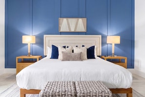 A bedroom with a large bed, two bedside tables, a headboard, and a wall-mounted artwork. - Luxury 5BR - Pool Game Room Mini Golf Fire Pit (Marco Island)