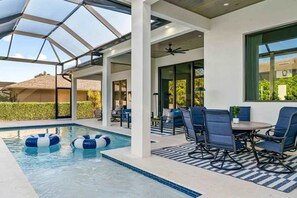 Zona de piscina exterior moderna con cerramiento de cristal, asientos y un ventilador de techo.
