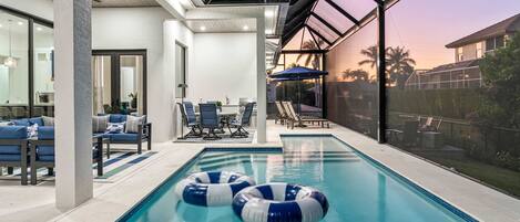 Une piscine intérieure dotée de deux toboggans, d’un espace détente avec des chaises et une table, et offrant une vue sur le coucher de soleil à travers une grande fenêtre.